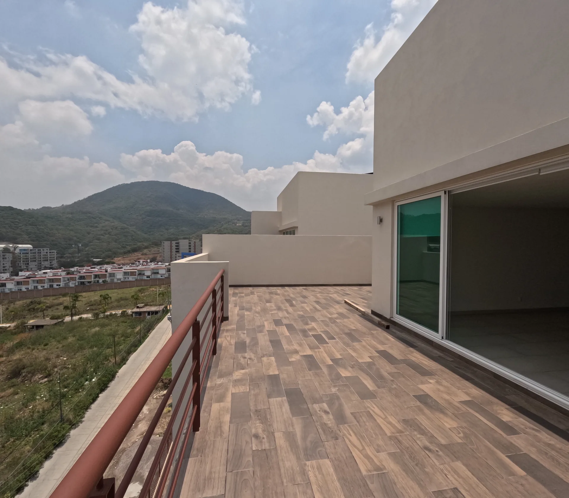 Terraza privada con piso tipo madera, barandal metalico rojo y vista a la montana y zona habitacional de Jilotzingo.