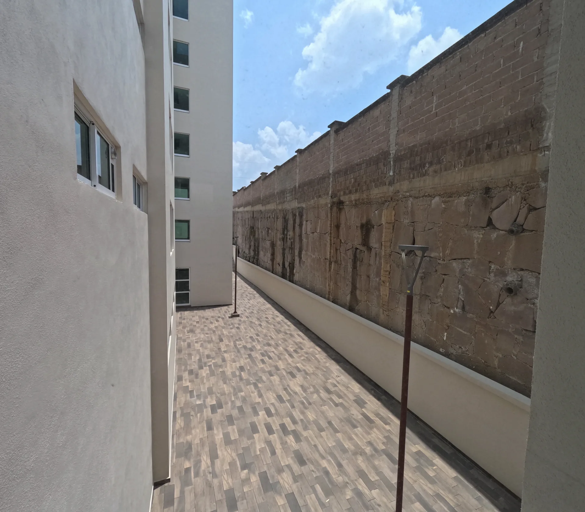 Pasillo exterior entre el edificio Residencial El Fraile y una pared de piedra del terreno colindante, con piso tipo madera.