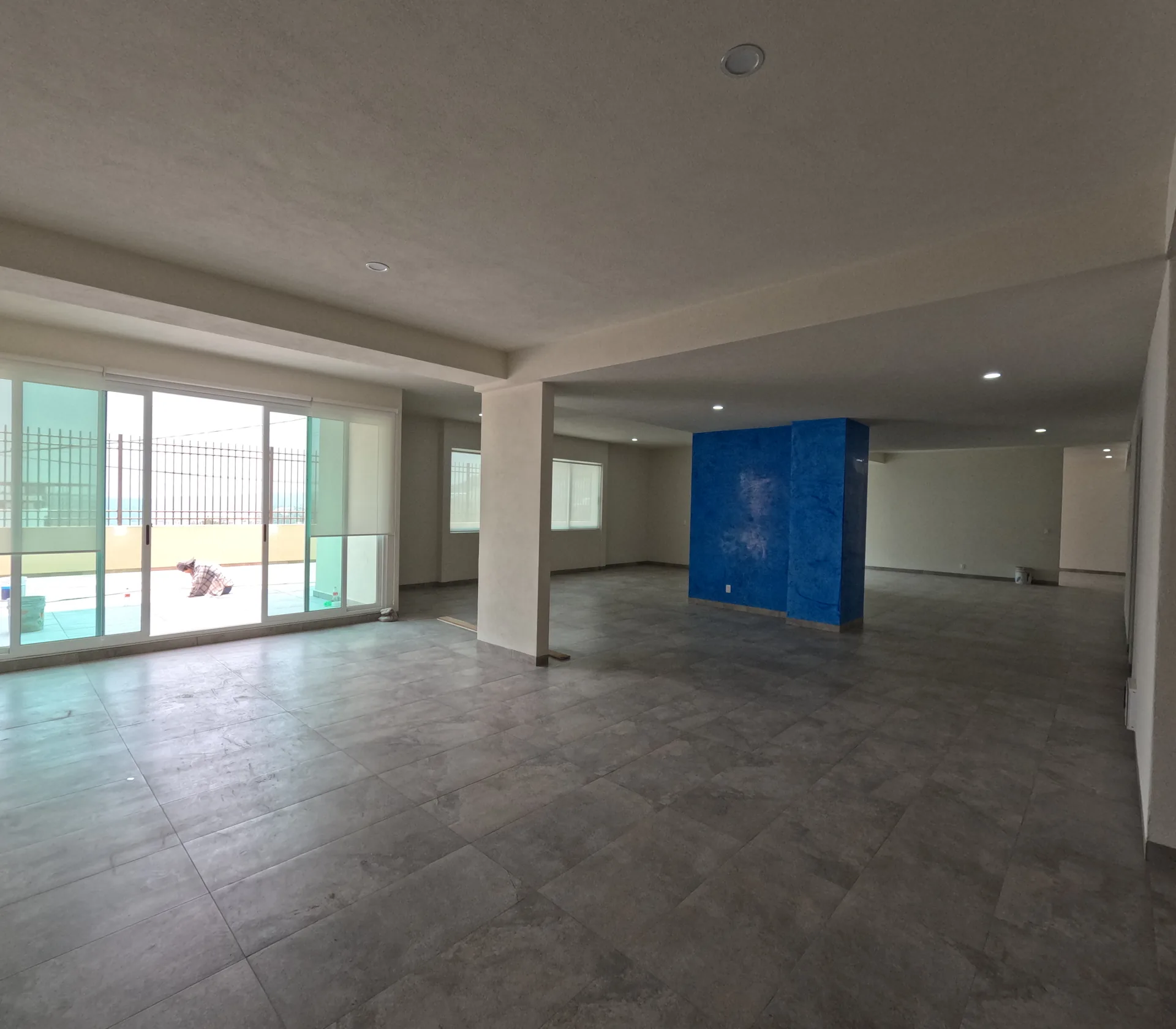 Salon de usos multiples en planta baja con piso de concreto pulido, columnas y ventanales hacia el exterior.