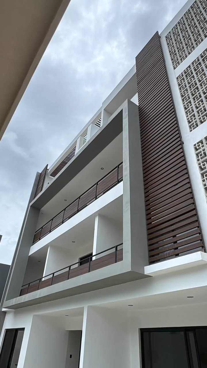 Fachada exterior de Itzae vista en contrapicada contra el cielo: balcones, celosías del edificio vecino y barandales de madera.